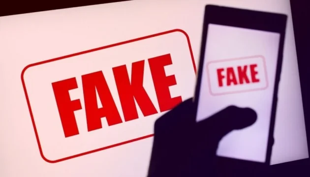 Силует руки зі смартфоном на тлі монітора з червоним штампом FAKE